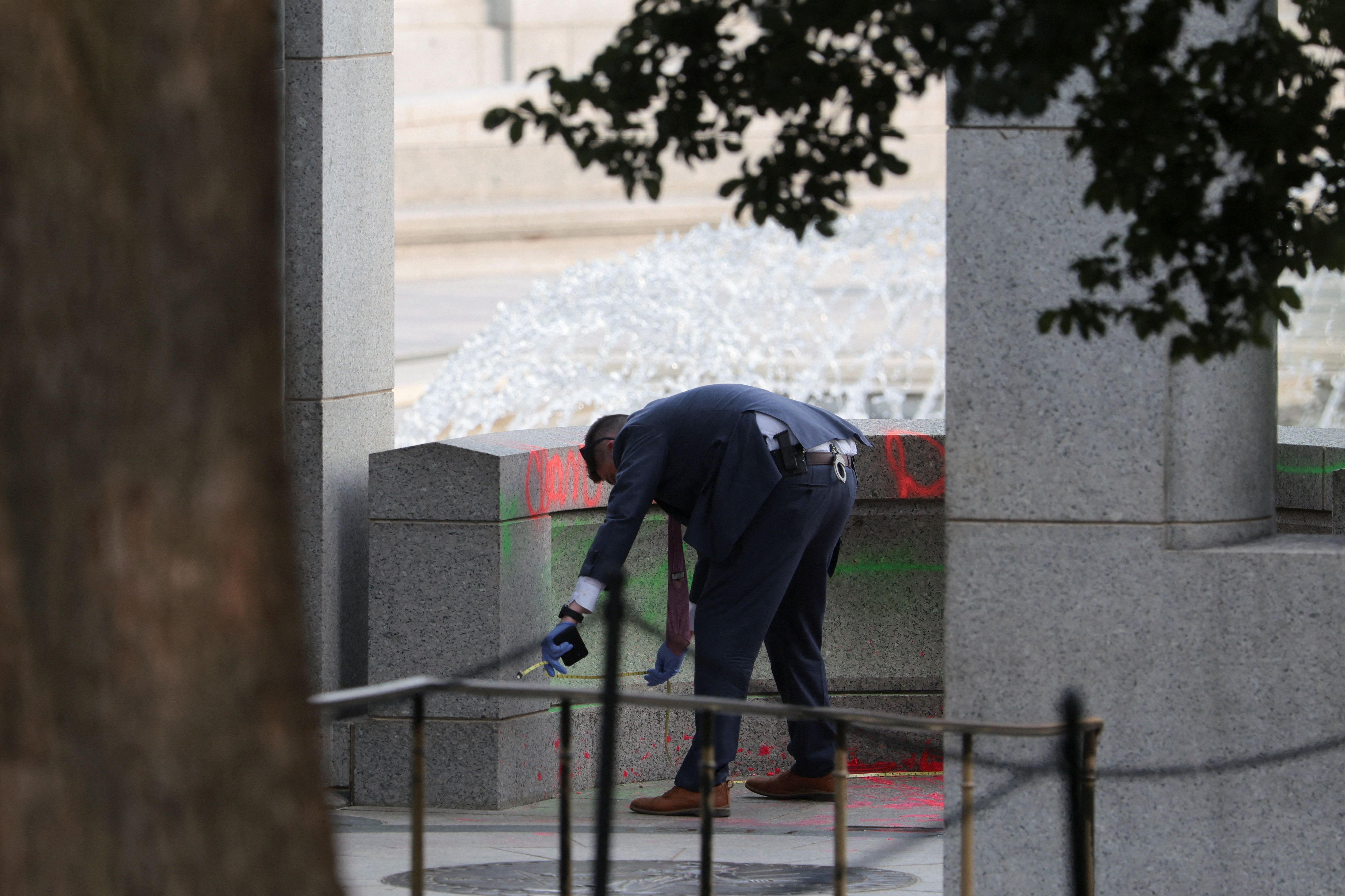 An investigator works at the World War II Memorial after the pool was reportedly vandalized with soap and graffiti on Aug. 13, 2026. - Kylie Cooper/Reuters
