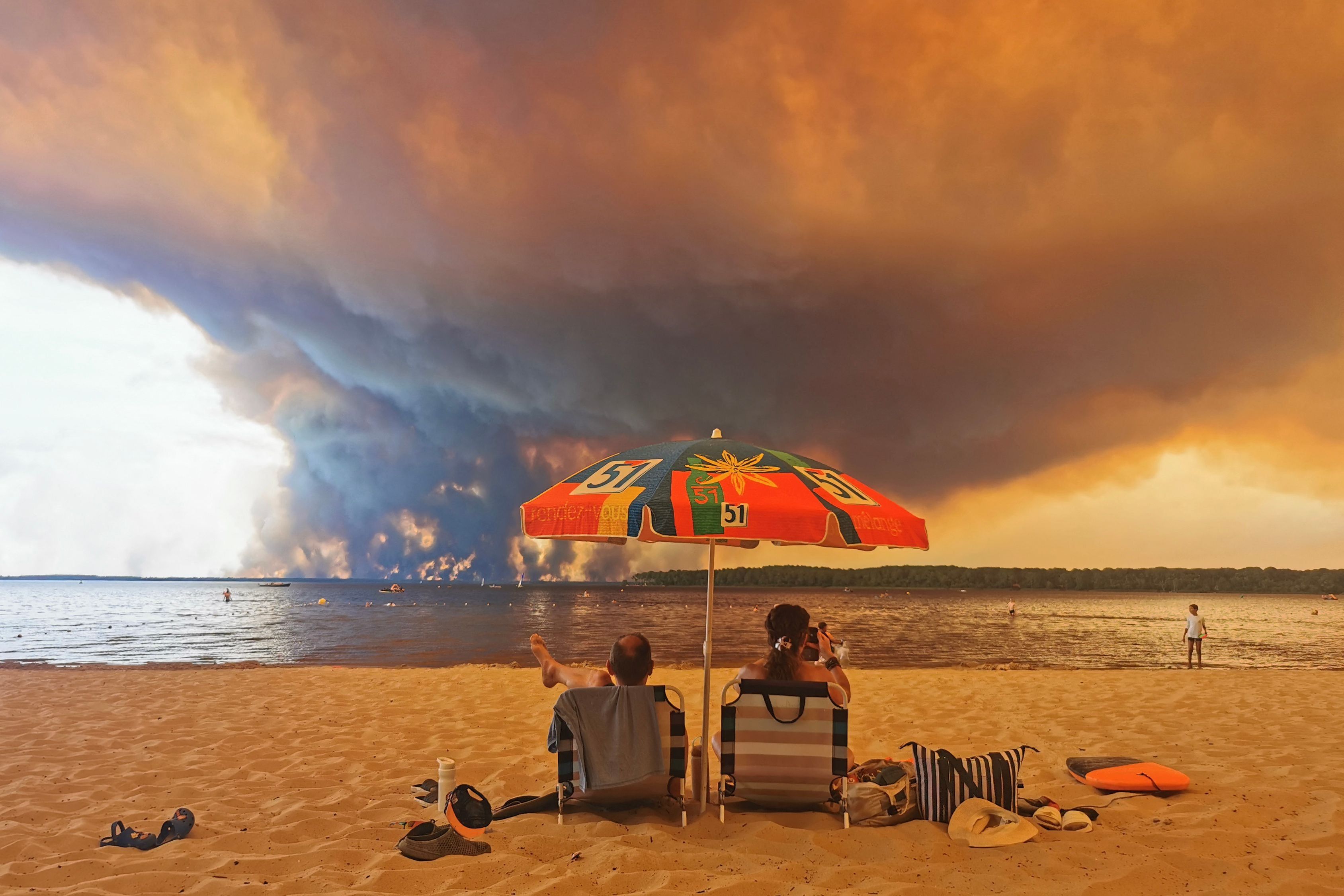 Beachgoers sit on a beach in Lacanau, southwestern France, as smoke from a wildfire rises on July 24, 2026. - Maximilien LAMY / AFP