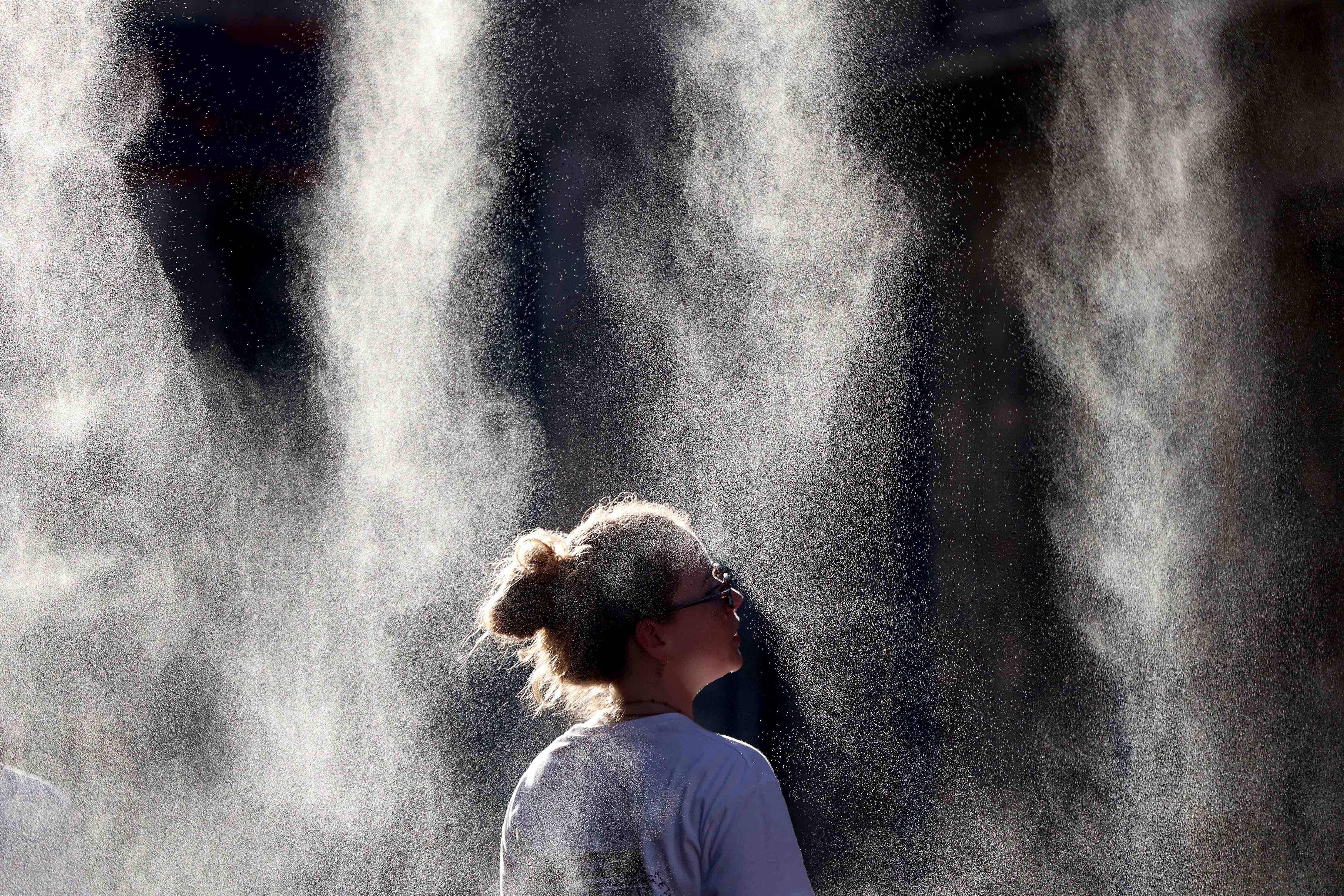 A woman cools off under a mist sprayer during a heatwave in Bordeaux. - AFP