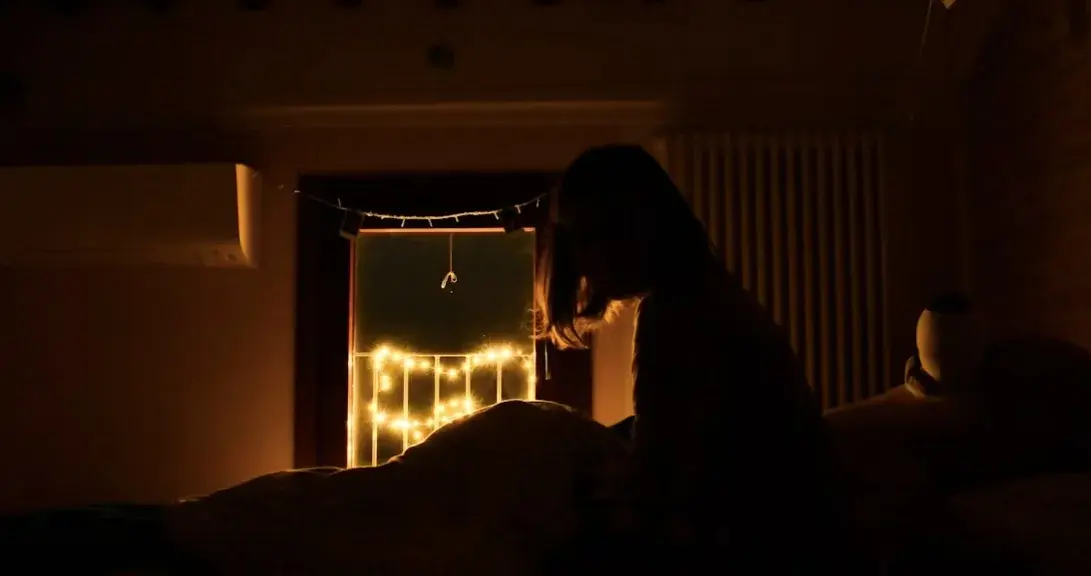 A person sits in bed as light from outside enters the room at night. - Unsplash