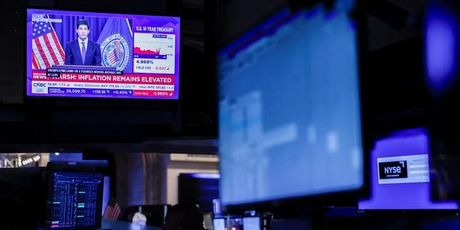A trader works on the New York Stock Exchange floor as screens show Kevin Warsh’s press conference after the Fed announcement. - lemonde.fr